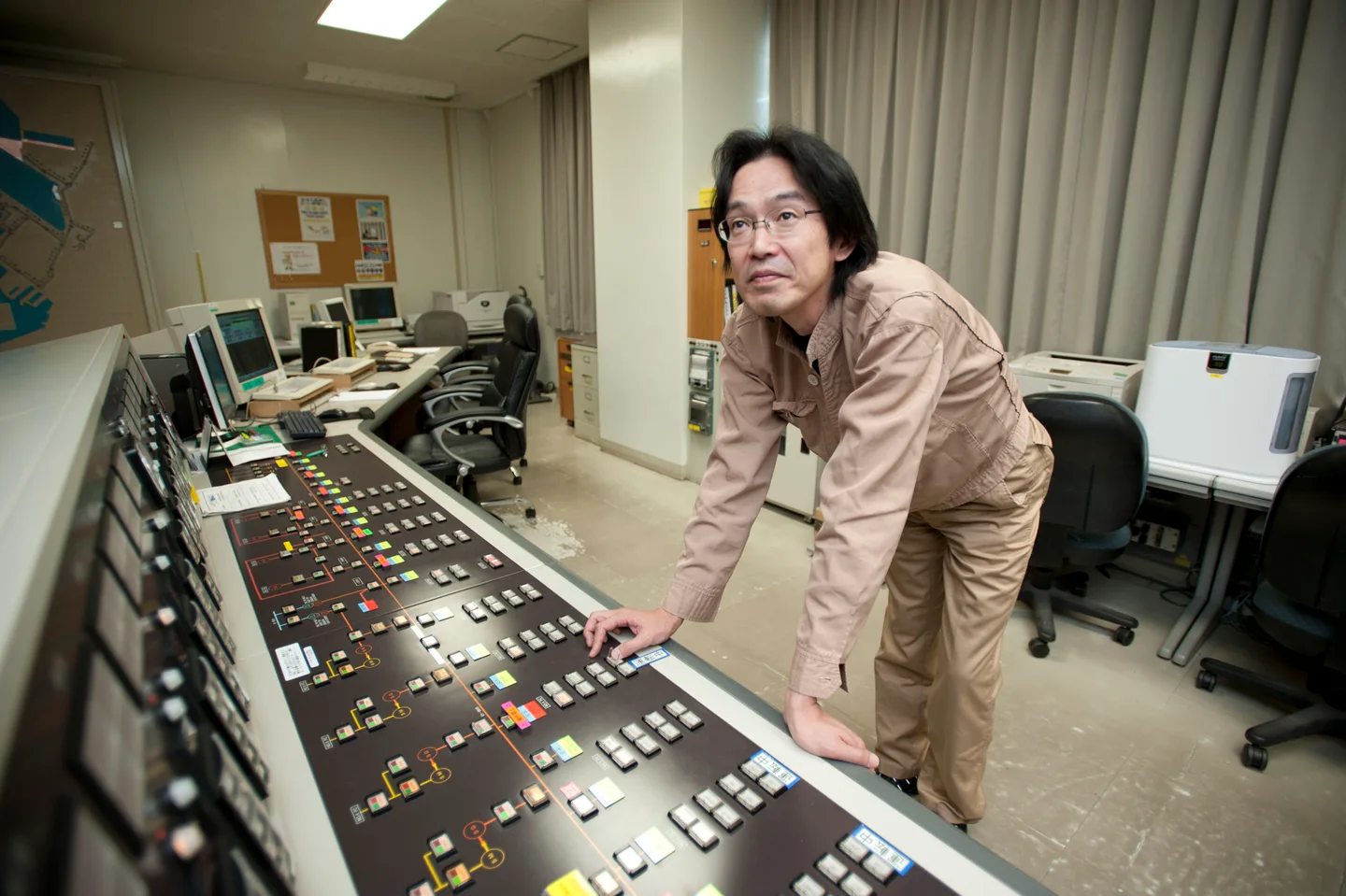 Operator in an energy control room with a synoptic panel and SCADA supervision stations in Yokosuka